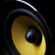Close-up view of gold meshed speaker bass driver enclosed in a black cabinet.