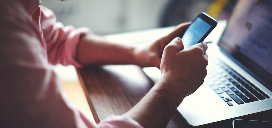 person using a smartphone by an open laptop