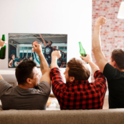 A group of three men watching a basketball game on the TV and cheering.