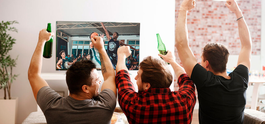 A group of three men watching a basketball game on the TV and cheering.